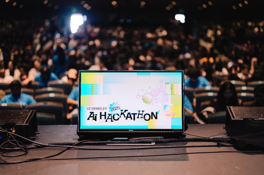 The AI Hackathon 2025 stage monitor facing a packed auditorium